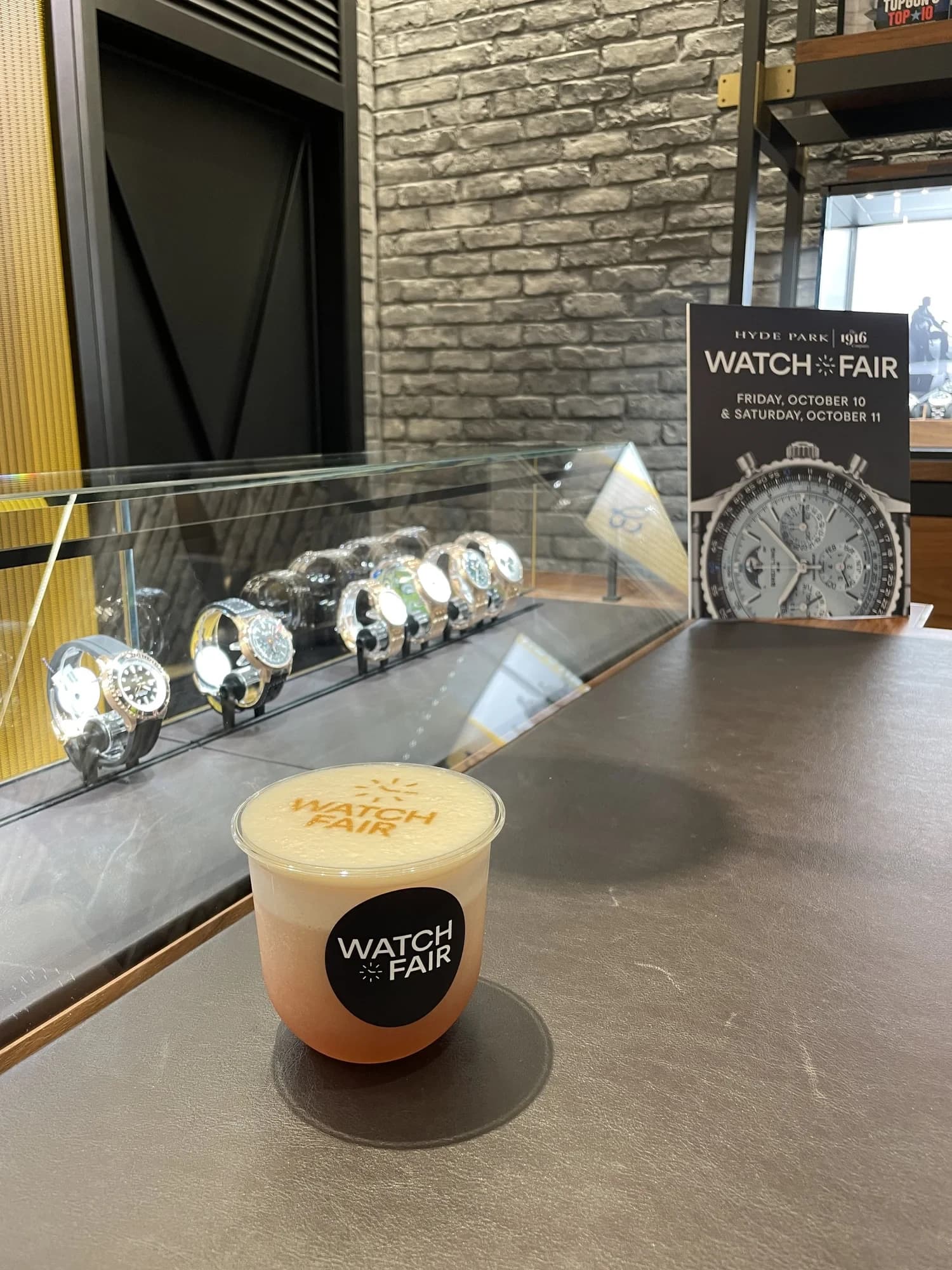 Latte printed with the Watch Fair logo beside a watch display case