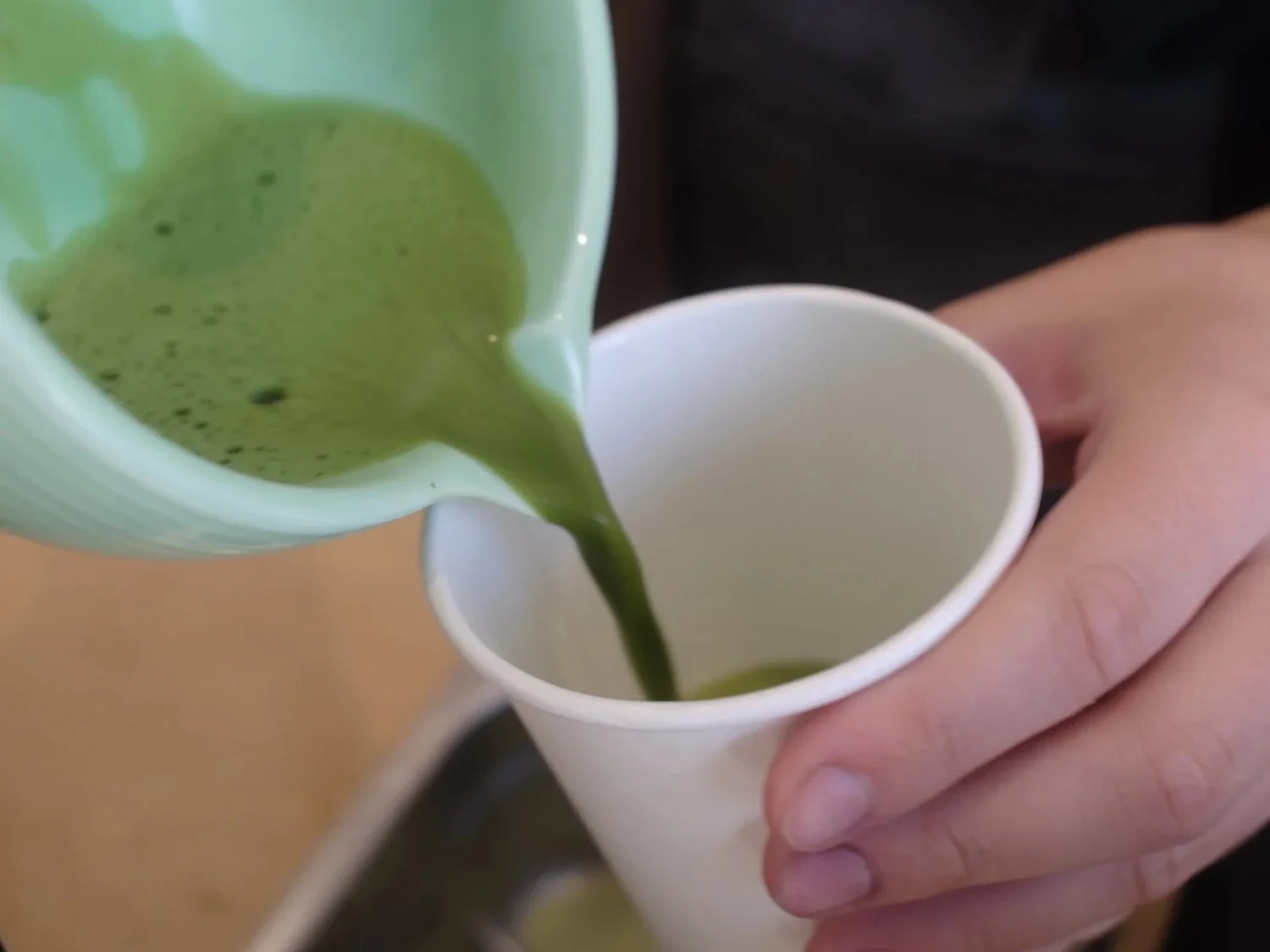 Barista pouring bright green matcha into a white cup
