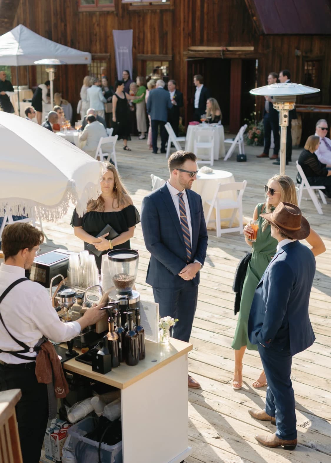 Wedding guests chatting at a Flipside espresso cart beside a mountain barn