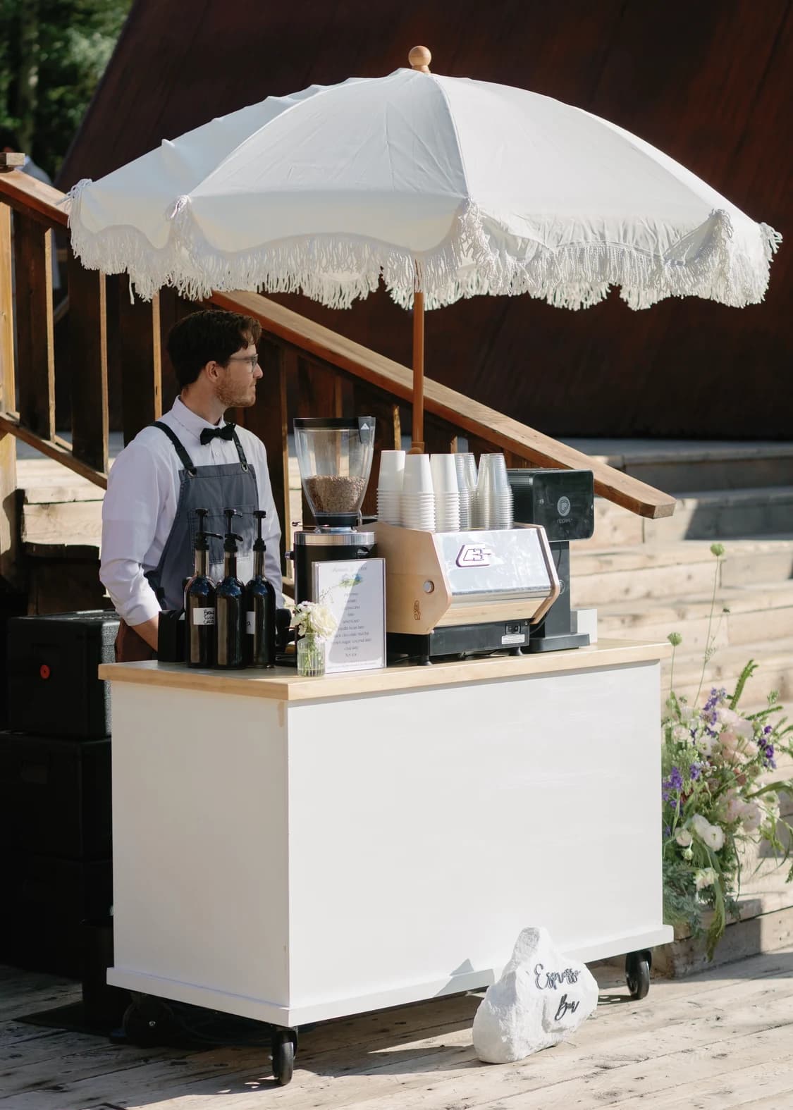 Flipside barista at a white coffee cart with a fringed umbrella at a mountain wedding