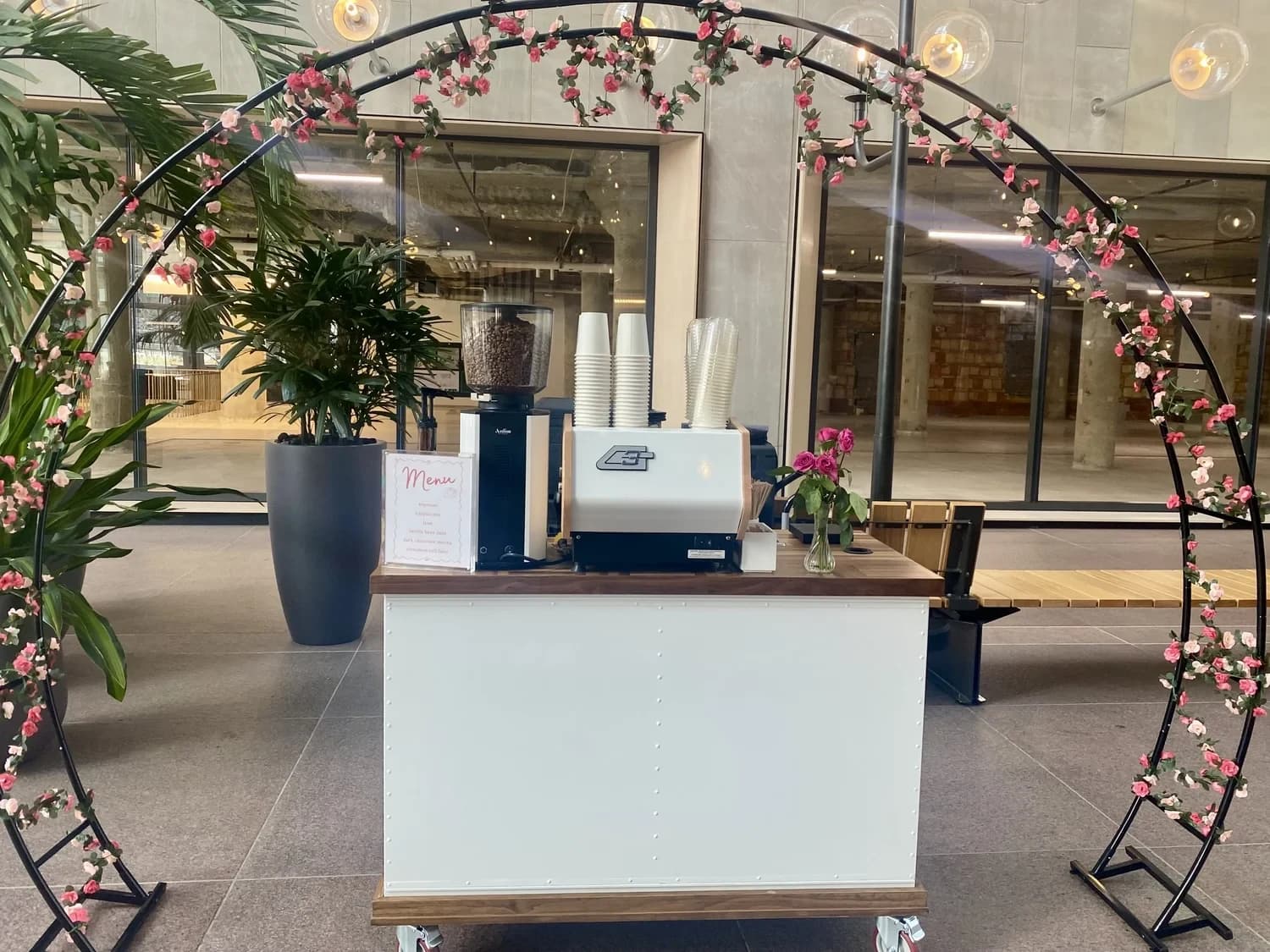 White Flipside coffee cart framed by a floral arch in a glass office lobby